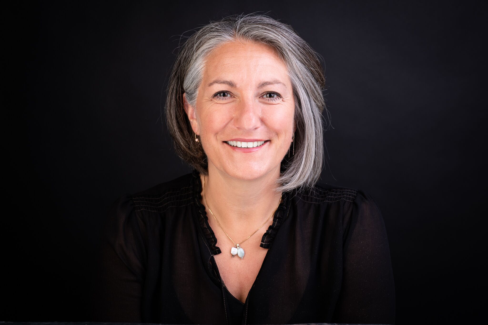A photo of a woman with short grey hair smiling widely and looking directly at the camera