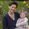 Victoria Robb and Matilda smile while sitting in a field surrounded by yellow flowers Matilda is holding a doll